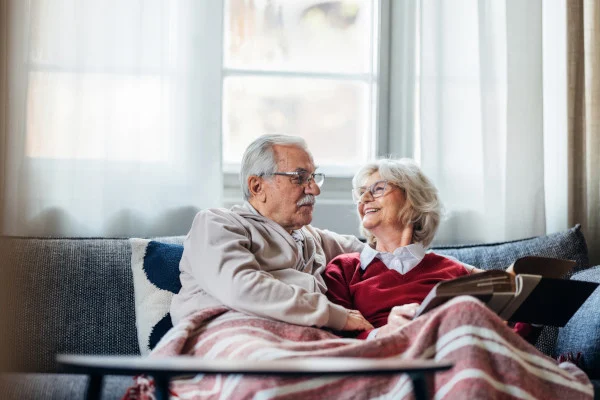 Two seniors enjoying a book together on the couch